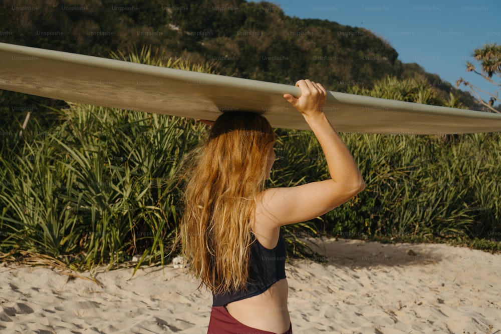 uma mulher segurando uma prancha de surf no topo de sua cabeça