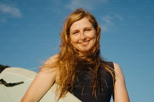 Una mujer sosteniendo una tabla de surf blanca bajo un cielo azul