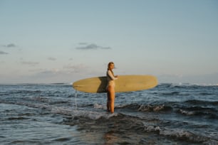 a woman standing in the ocean holding a surfboard