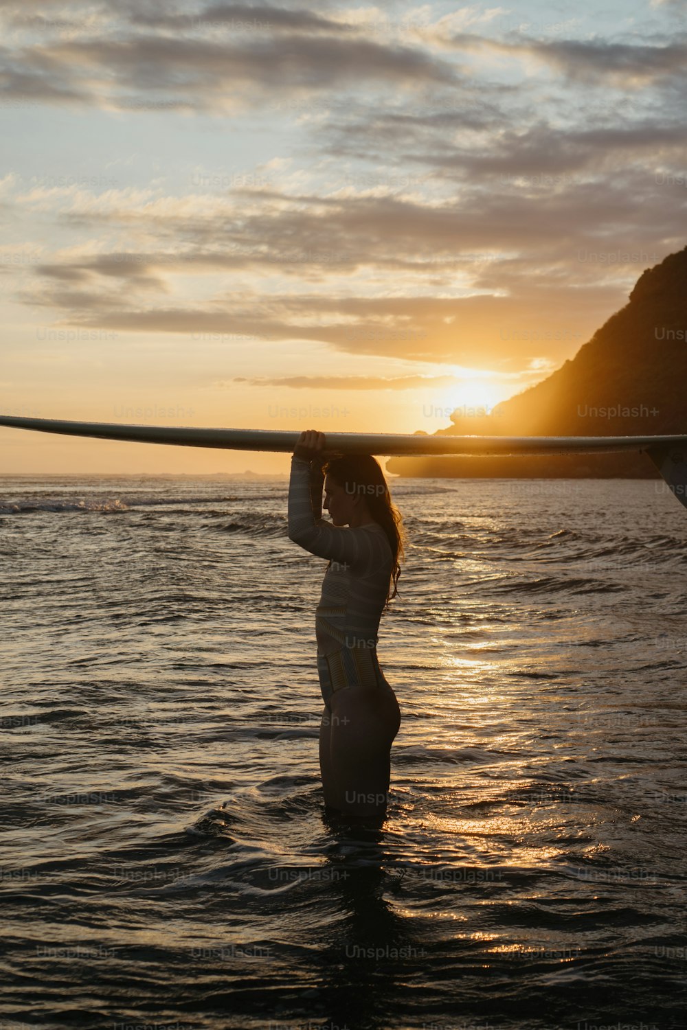 uma mulher em pé na água segurando uma prancha de surf sobre sua cabeça