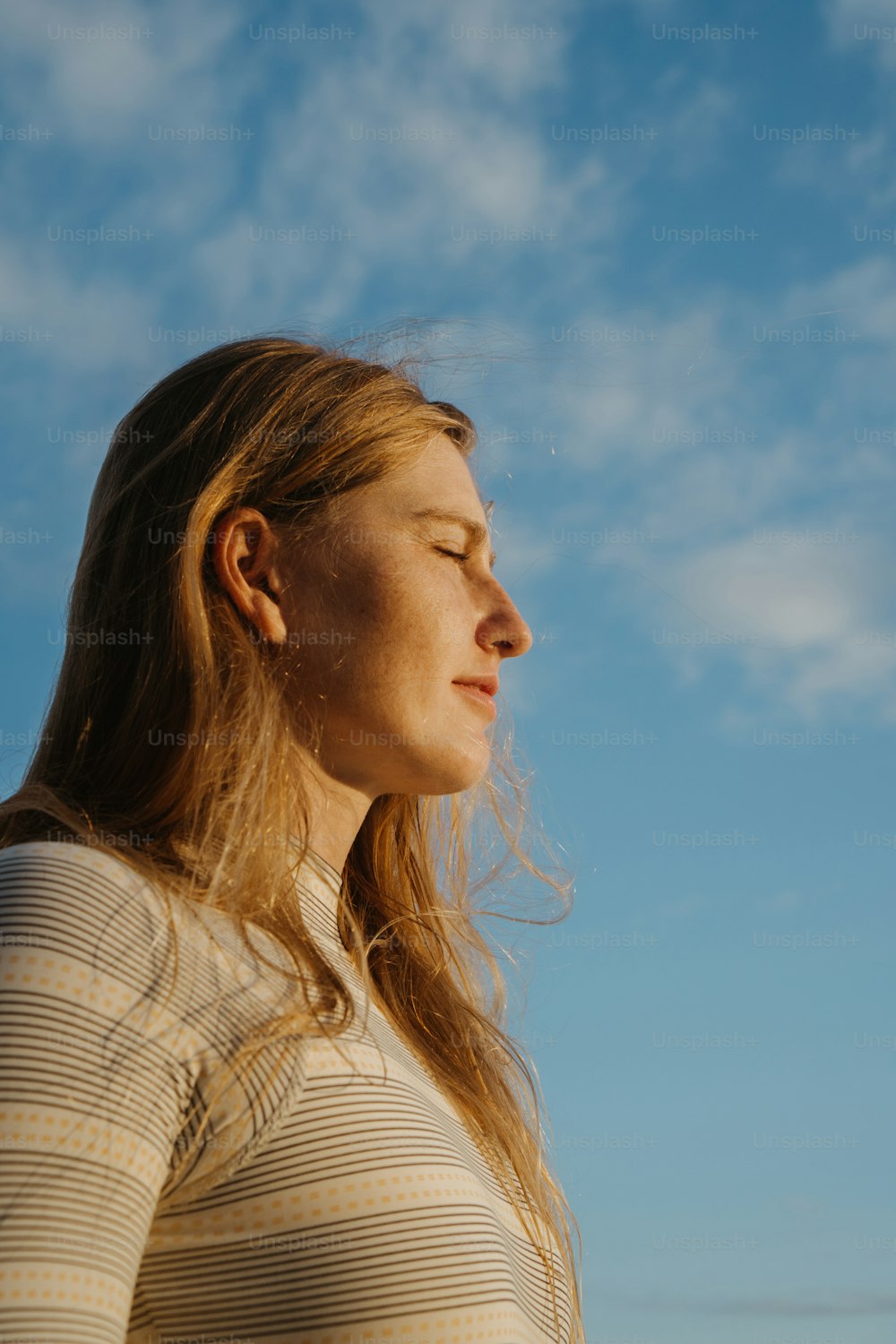 Una mujer con los ojos cerrados de pie frente a un cielo azul