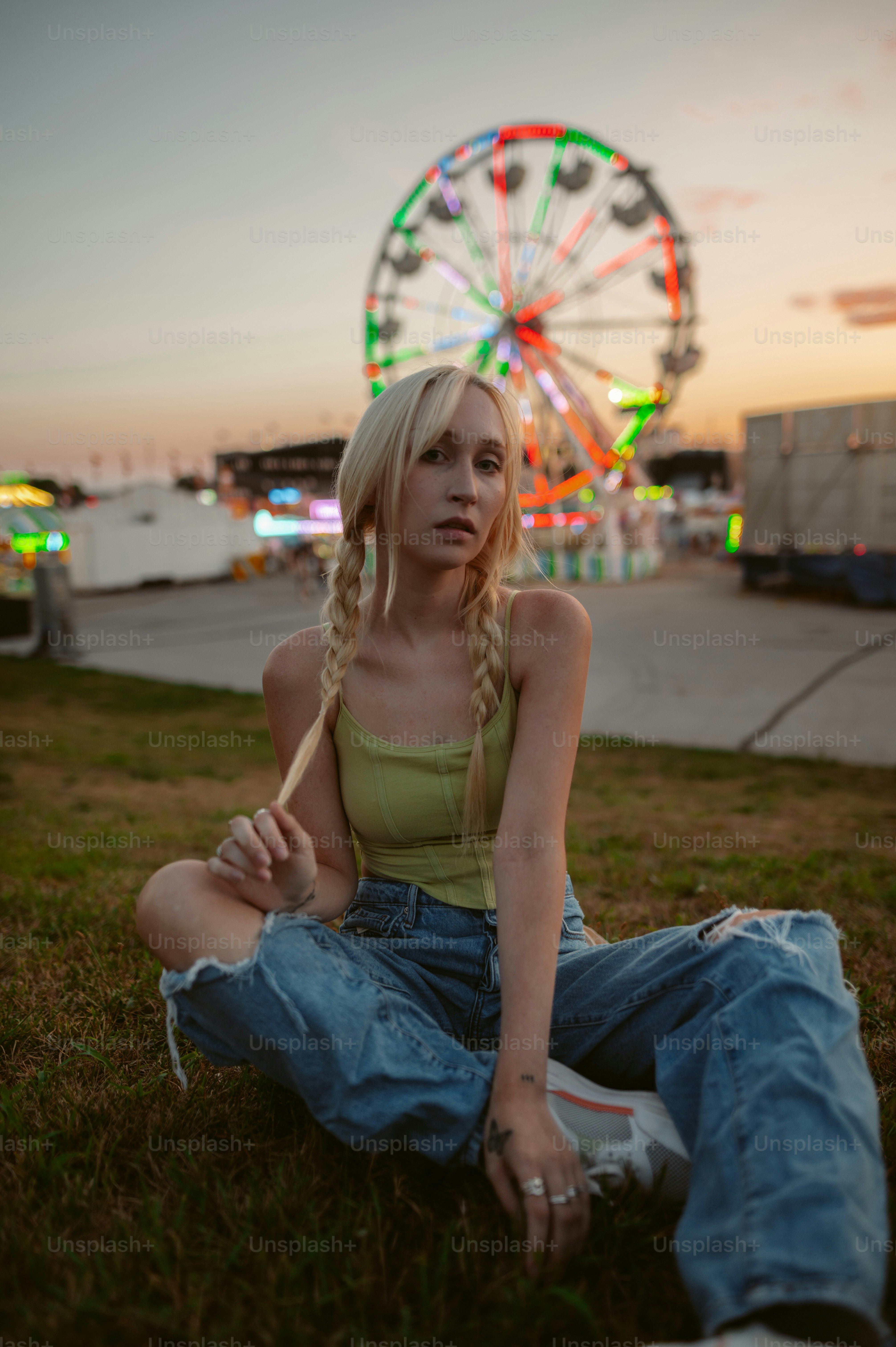 a woman sitting in the grass with a ferris wheel in the background