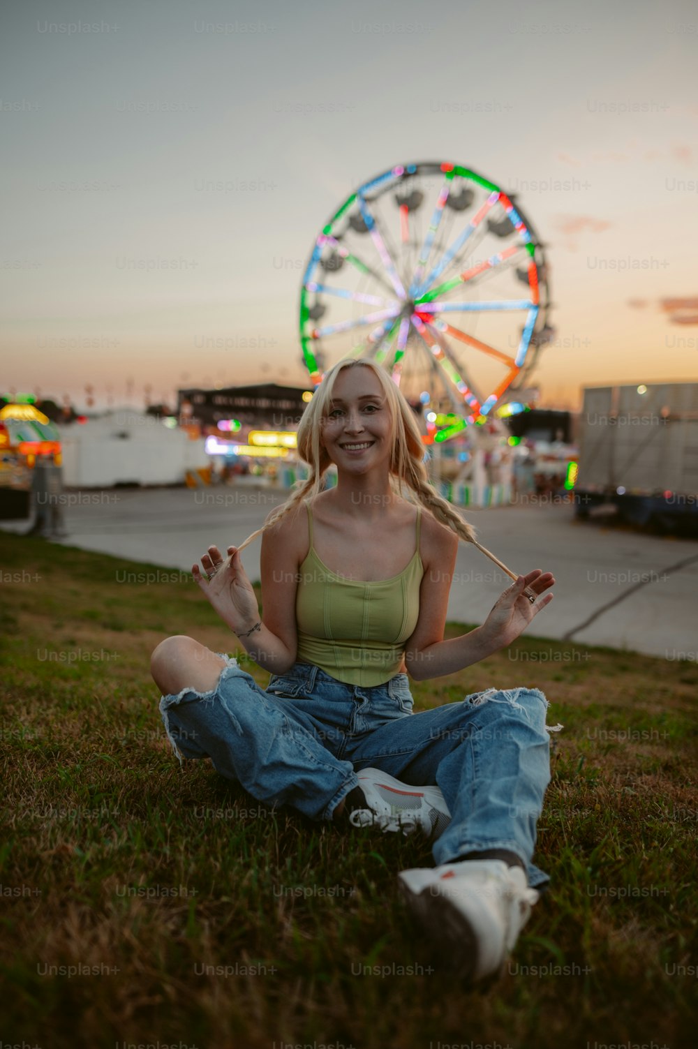 a woman sitting on the grass in front of a ferris wheel