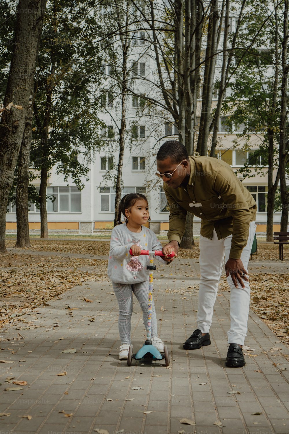 a man teaching a little girl how to ride a scooter