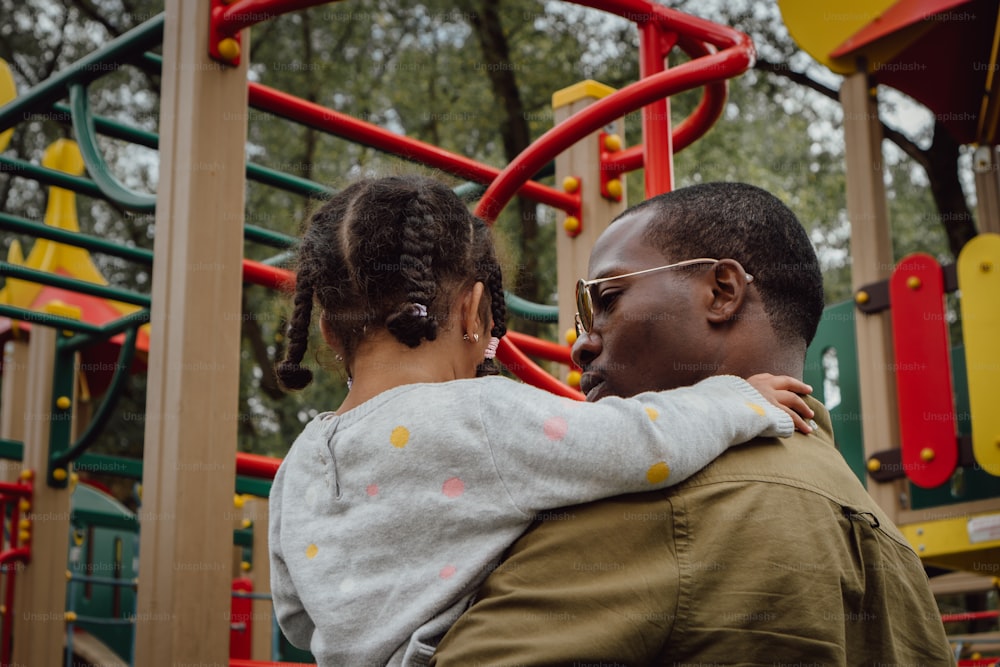 a man holding a little girl in front of a playground