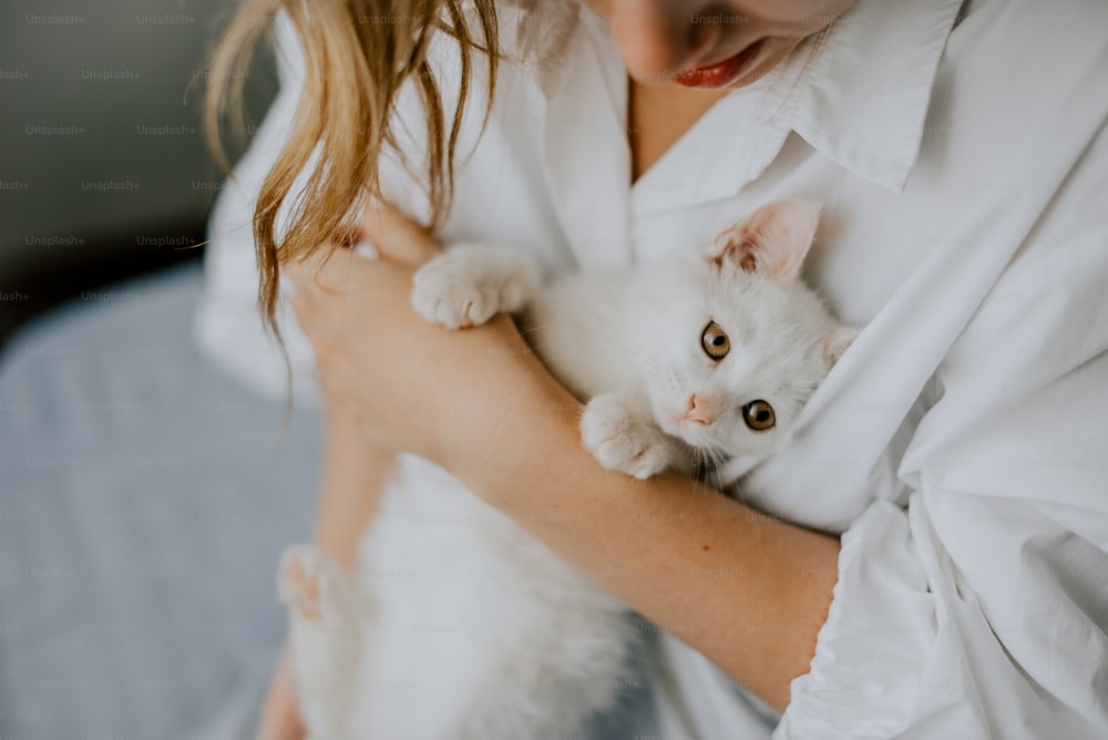 a woman holding a white kitten in her arms