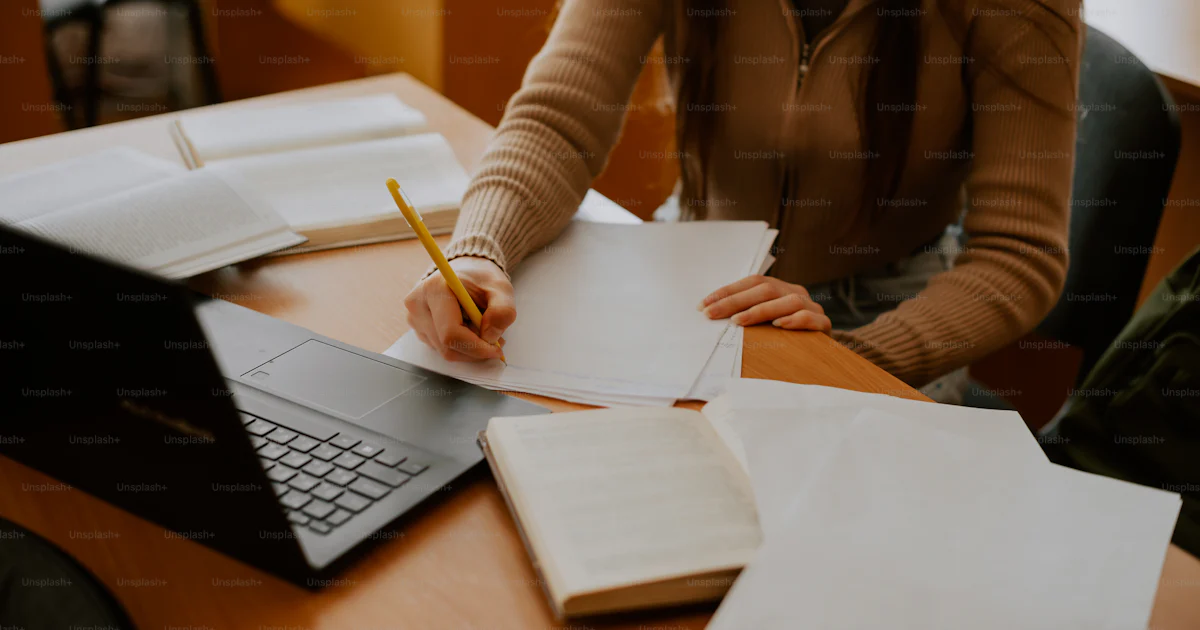 A woman sitting at a desk writing on a notebook photo – Library Image ...