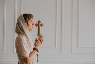 a woman wearing a veil and praying with a cross in the background