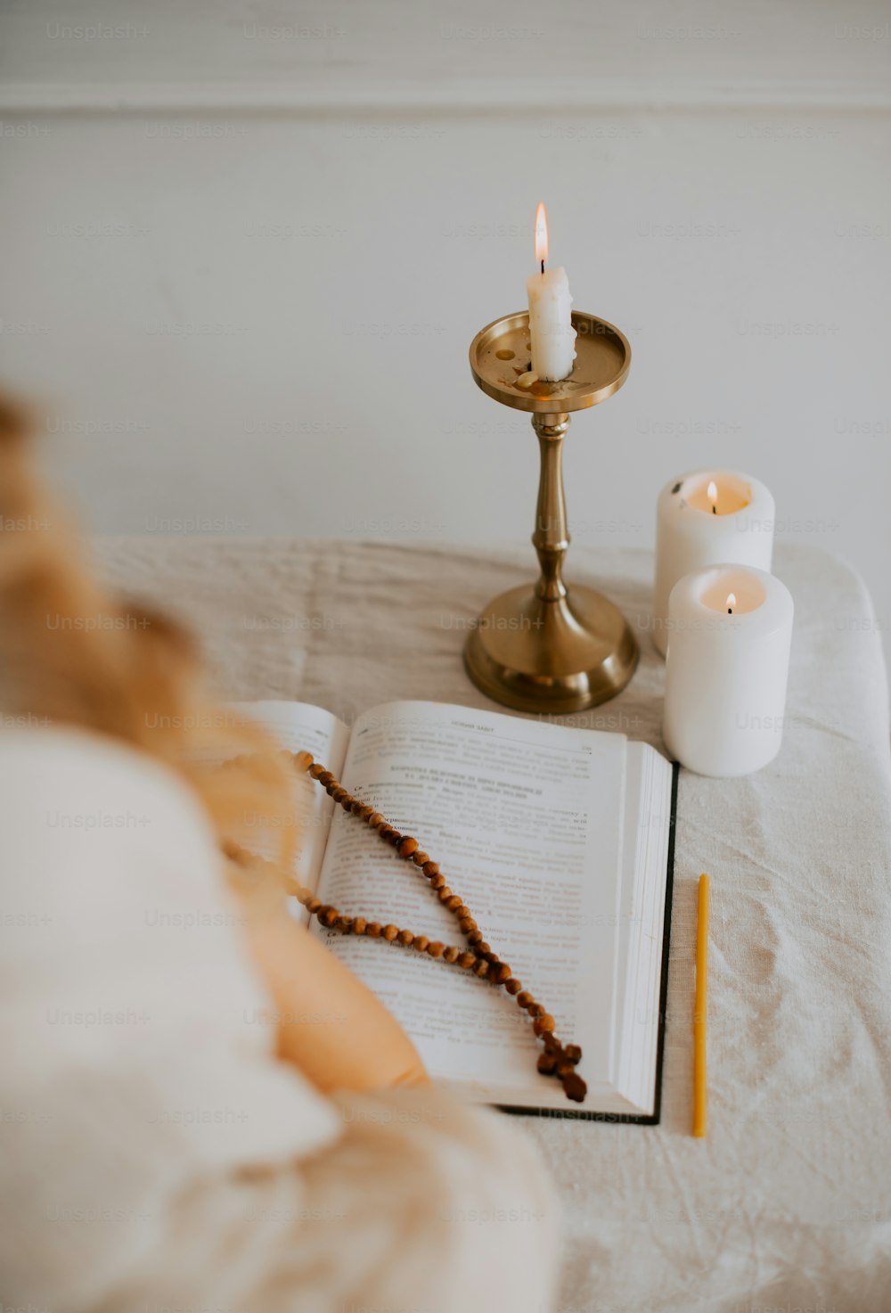 a candle, rosary, and book on a bed