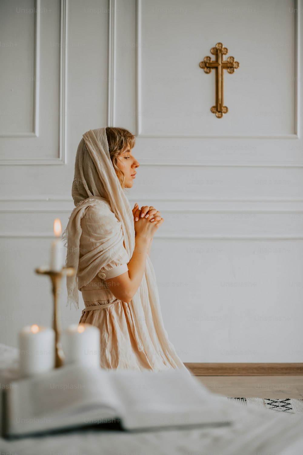 Une femme en robe blanche agenouillée devant une croix