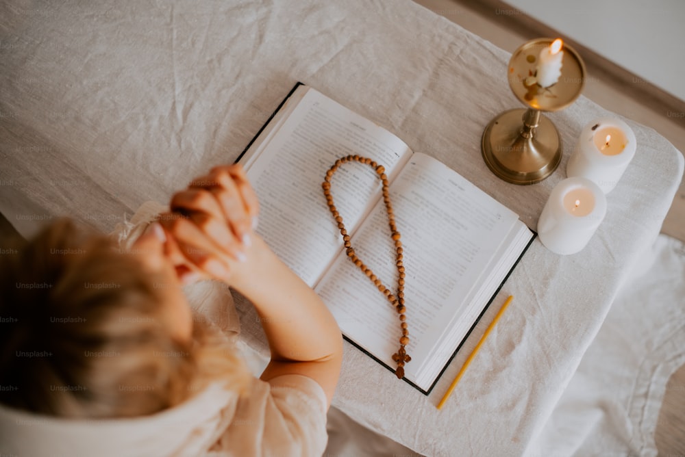 a little girl sitting at a table with a book and rosary