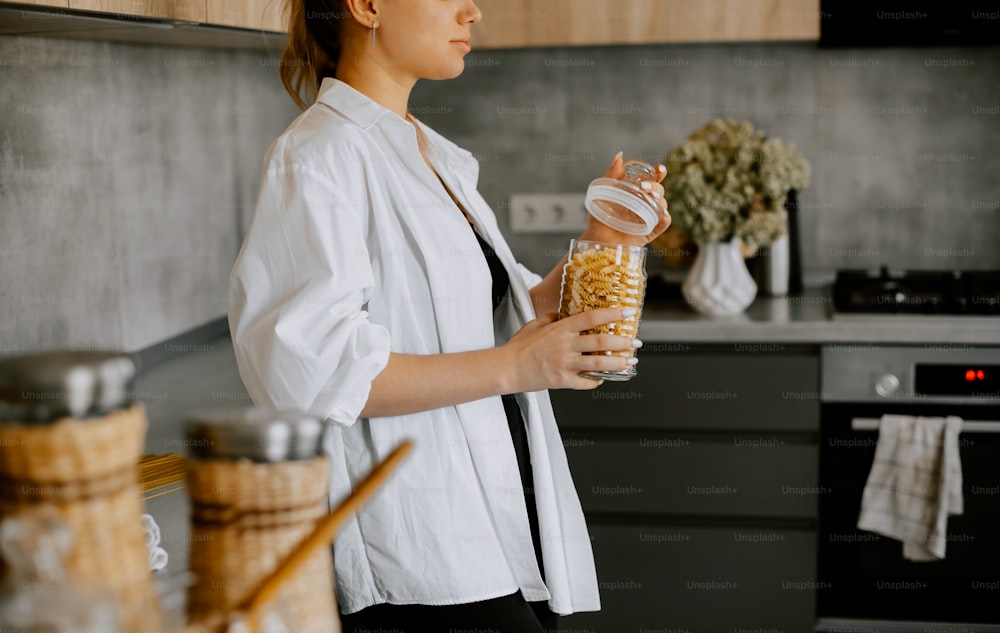 a woman standing in a kitchen holding a jar of cereal