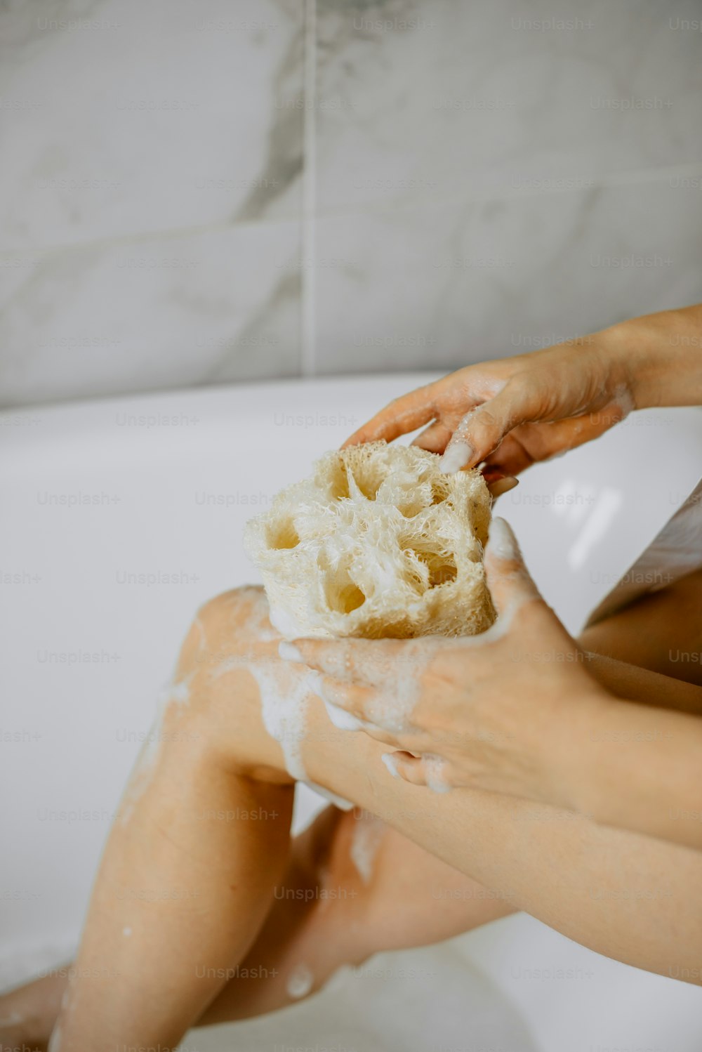 Una mujer sentada en una bañera sosteniendo una esponja