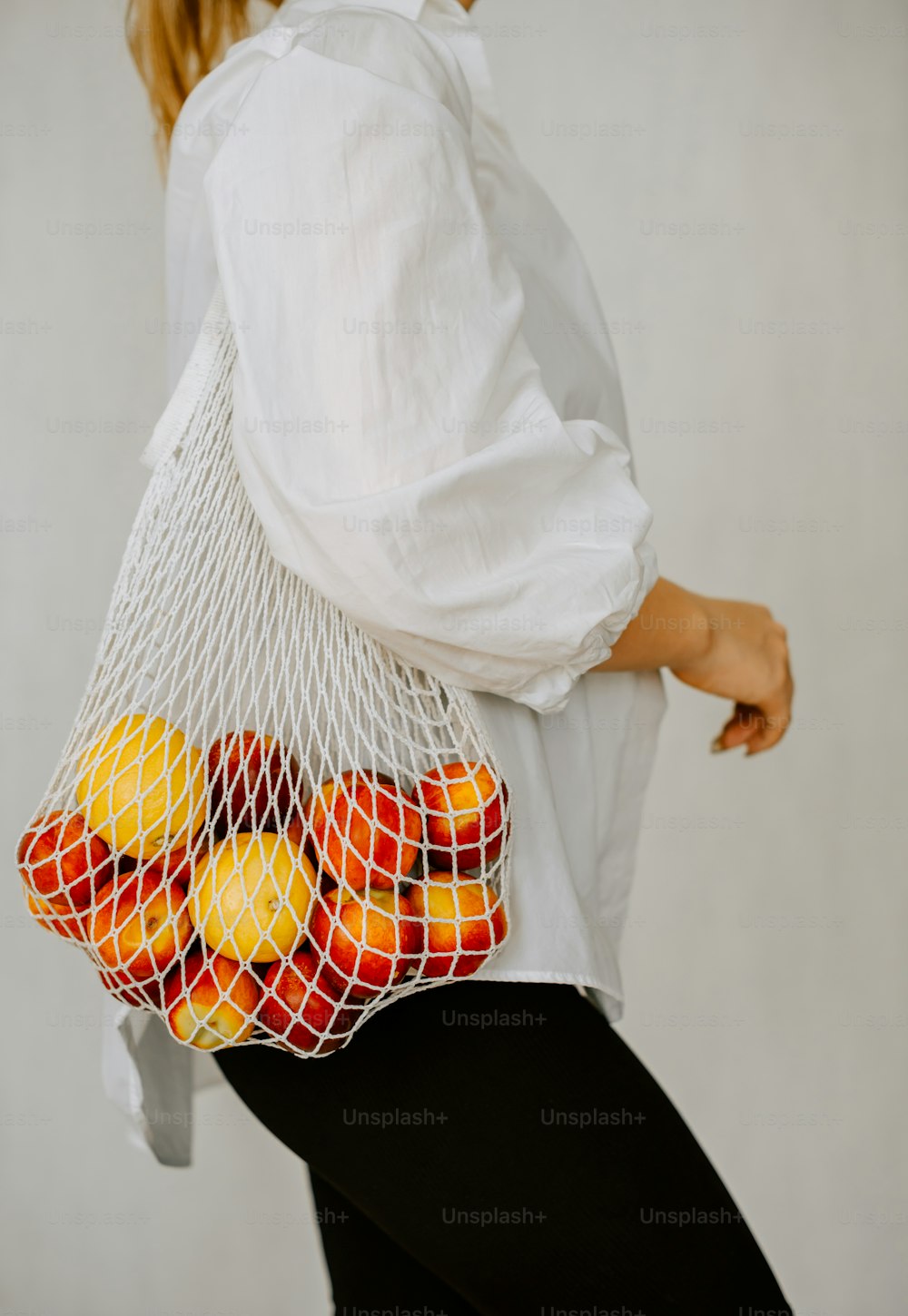 a woman carrying a mesh bag full of oranges