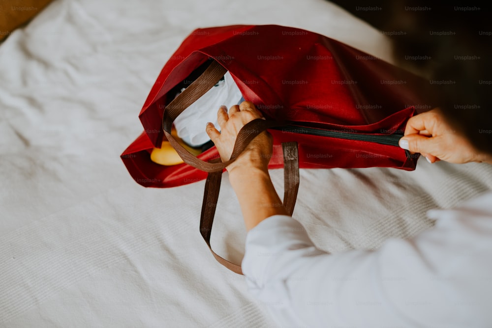 eine Person, die eine rote Tasche auf einem Bett hält