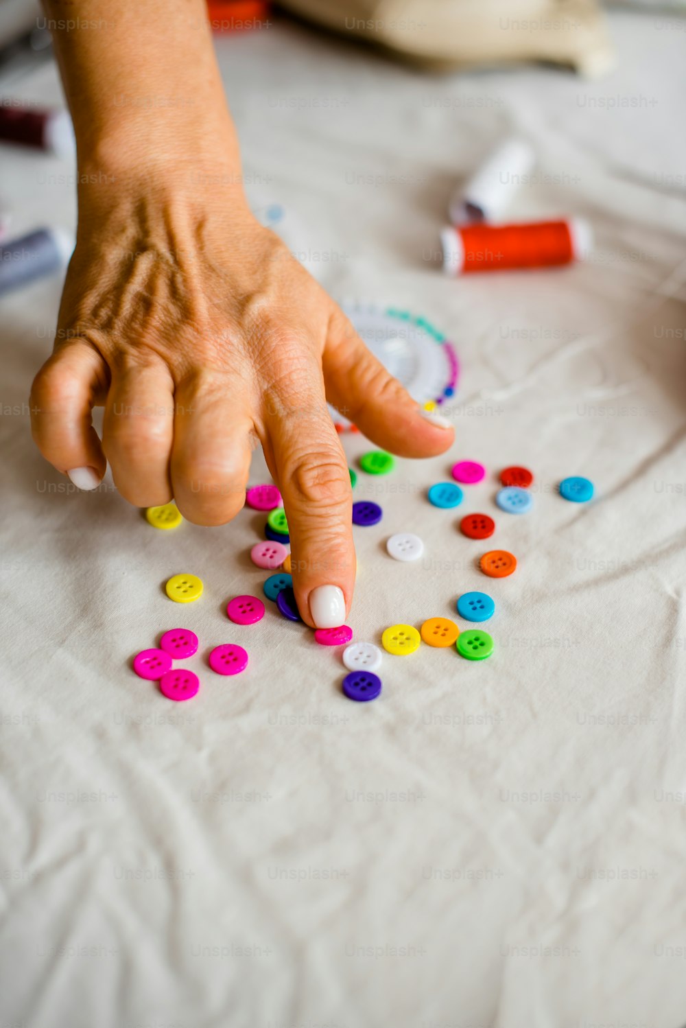 a person's hand reaching for colorful buttons on a table