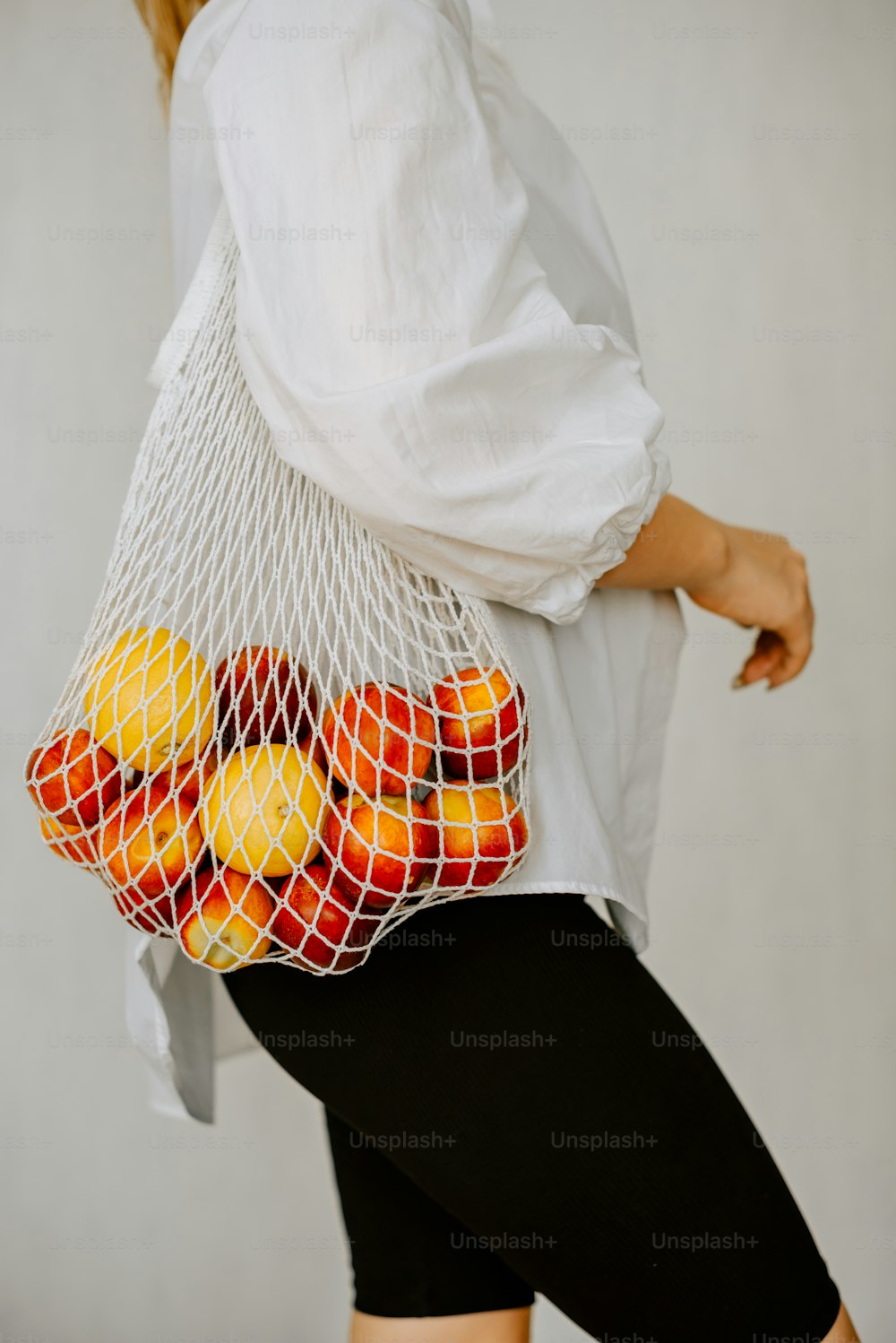 uma mulher carregando um saco de malha cheio de laranjas