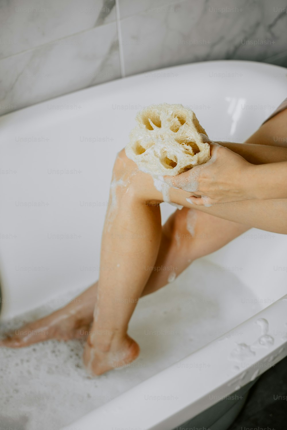 una persona sentada en una bañera con una esponja en la cabeza