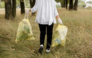 a woman walking through a field carrying two bags
