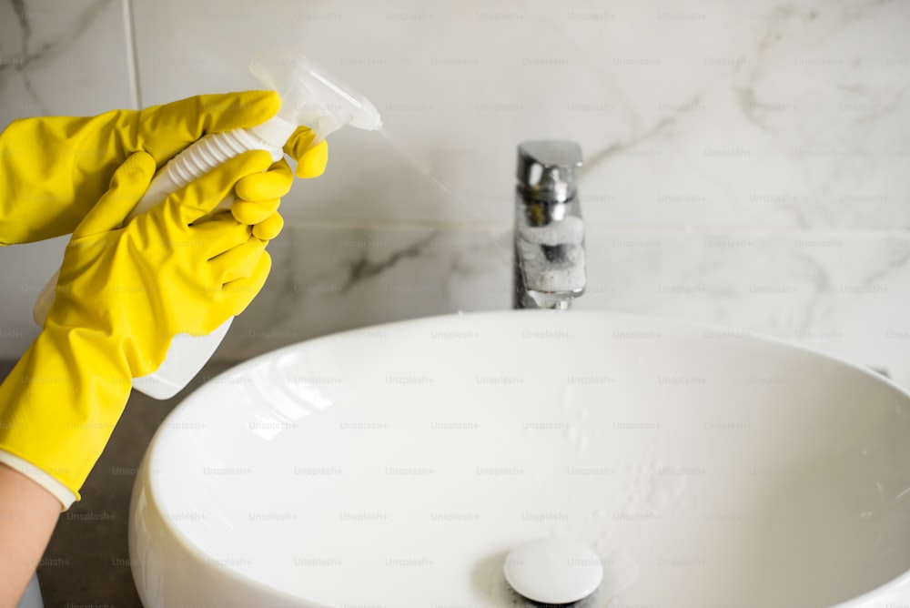 une personne portant des gants jaunes nettoie un évier blanc
