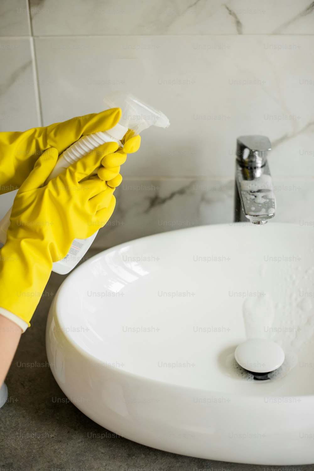 a person in yellow gloves cleaning a white sink