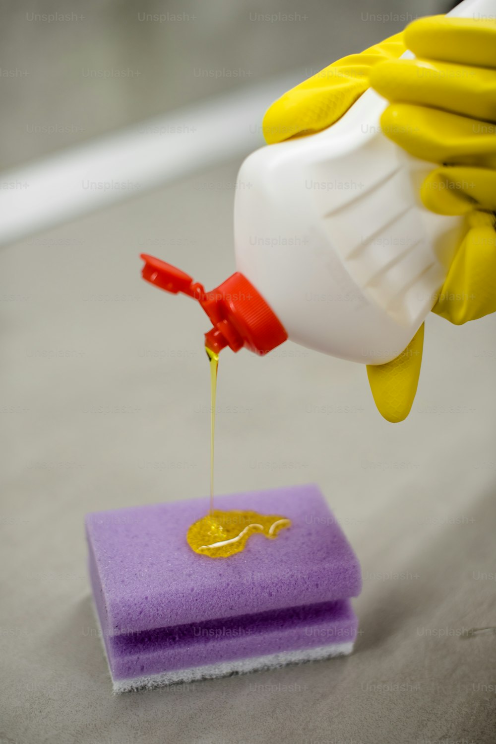a person in yellow gloves is pouring yellow liquid onto a sponge