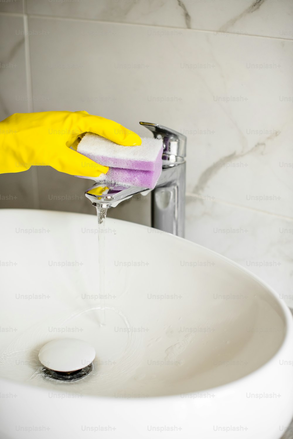 a person in yellow gloves is washing a white sink
