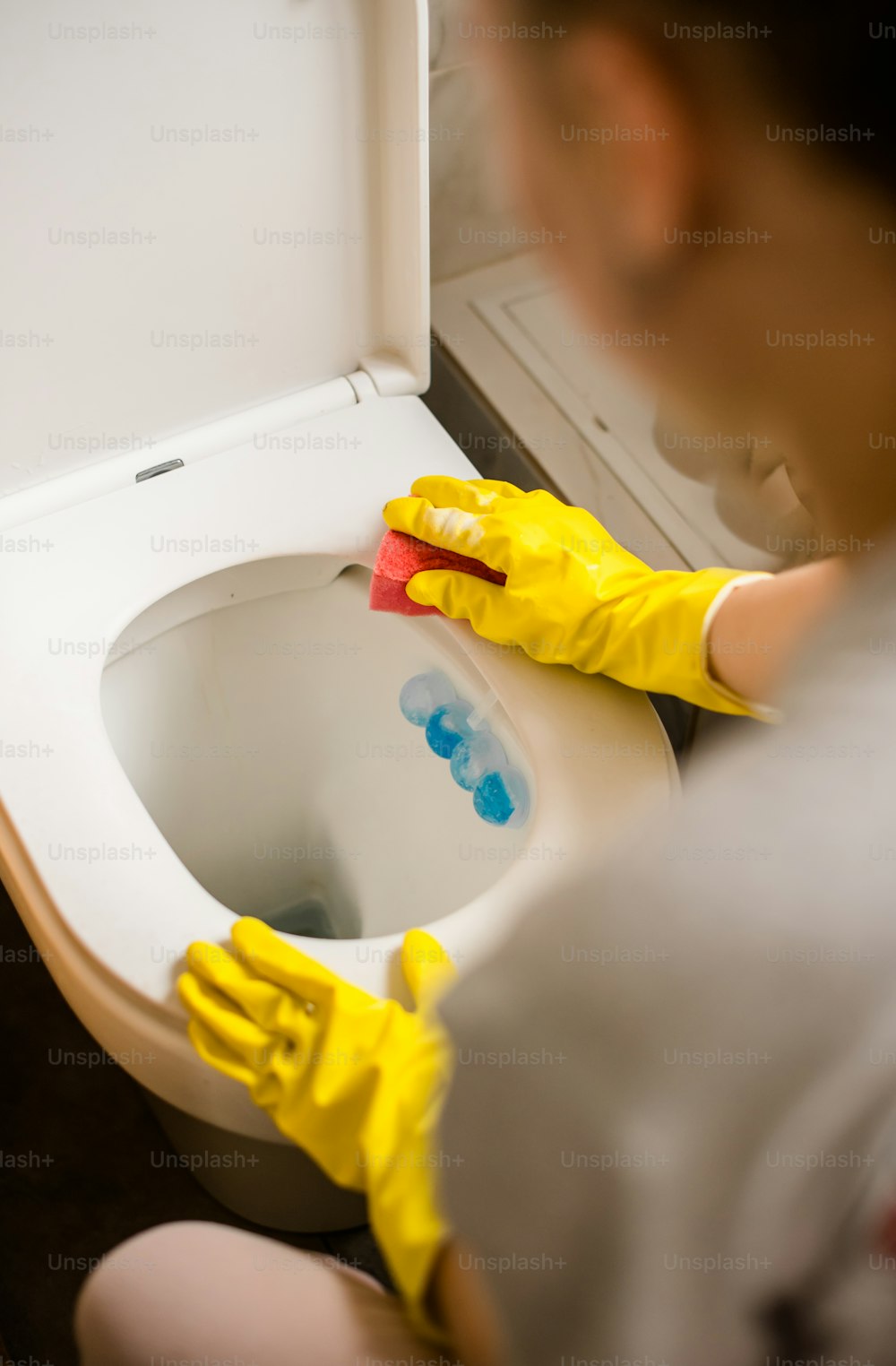 une personne portant des gants jaunes nettoyant une toilette