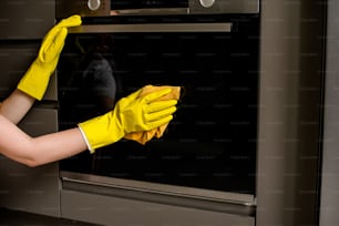 Una donna in guanti gialli che pulisce un forno