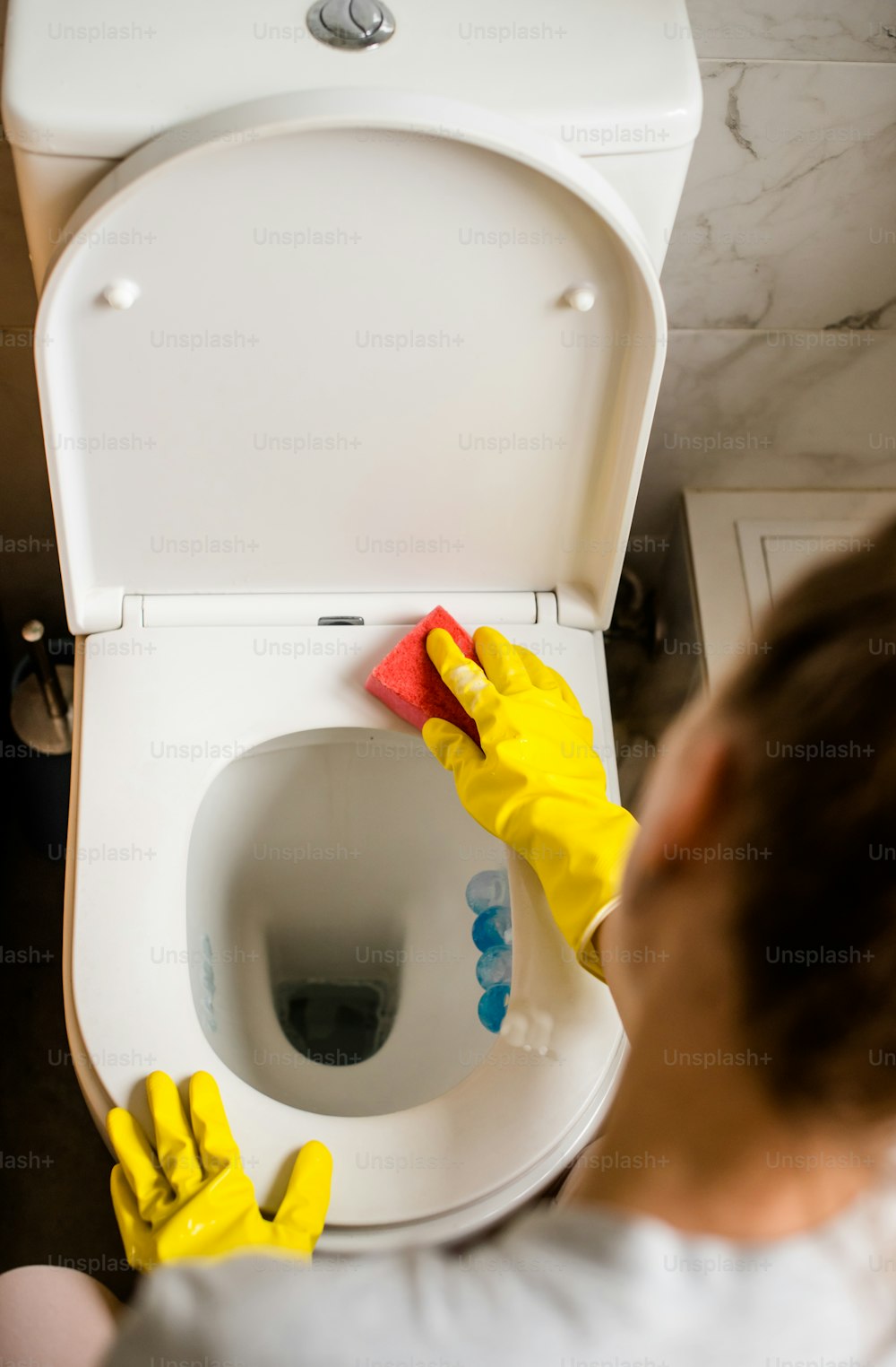 eine Person in gelben Handschuhen, die eine Toilette putzt