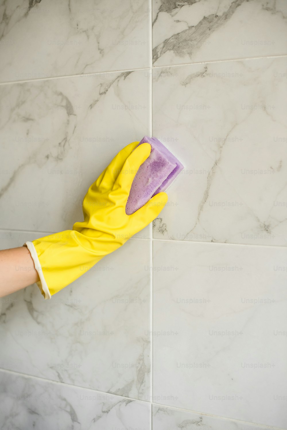 a person's hand with a yellow glove on a tile wall