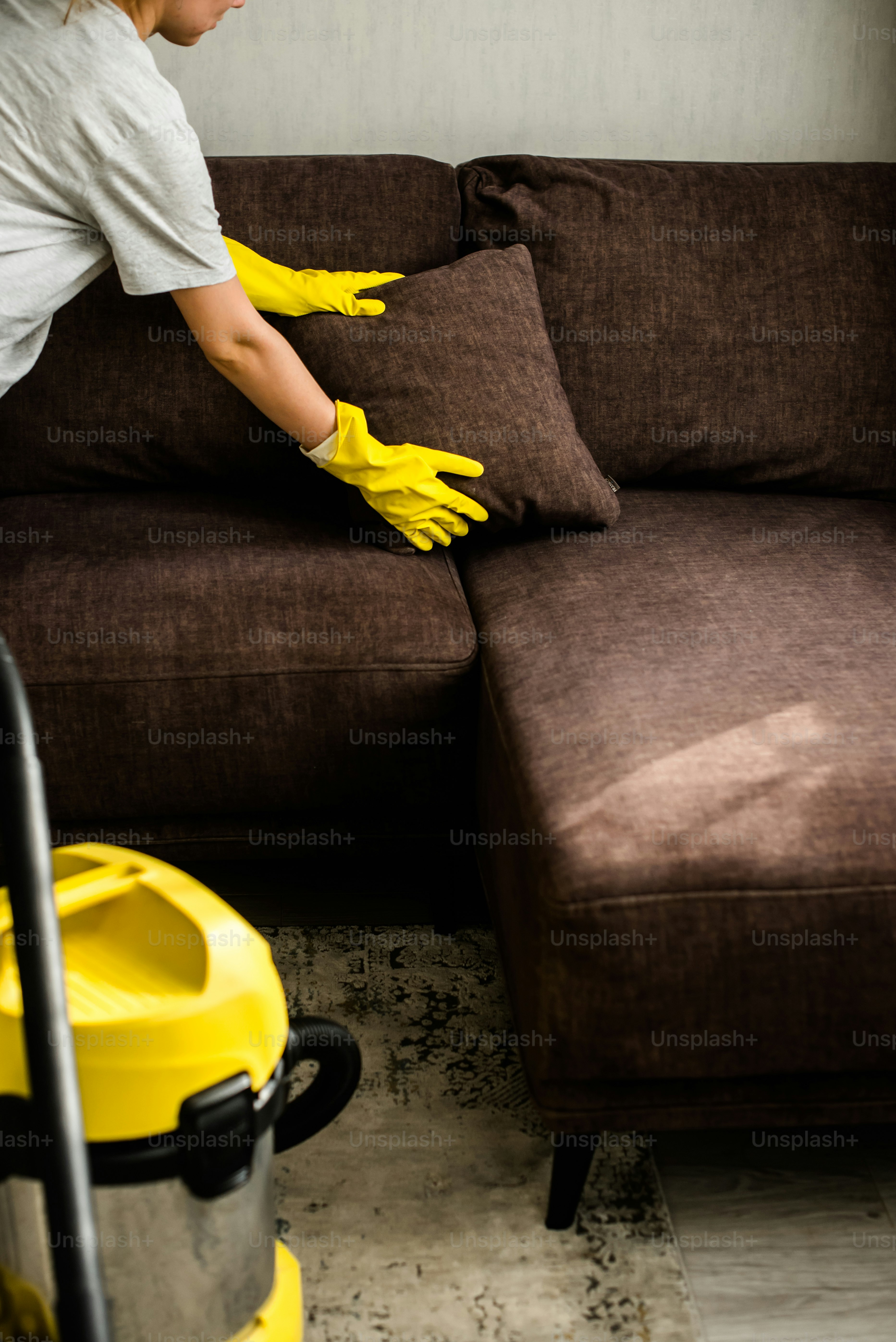 a woman cleaning a couch with yellow gloves