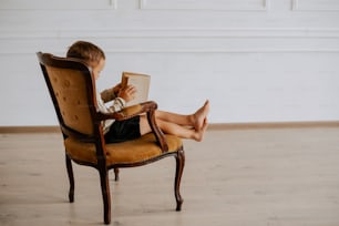 a young boy sitting in a chair reading a book