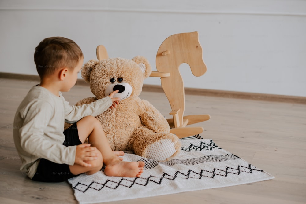 Ein kleiner Junge, der mit einem Teddybären auf dem Boden sitzt