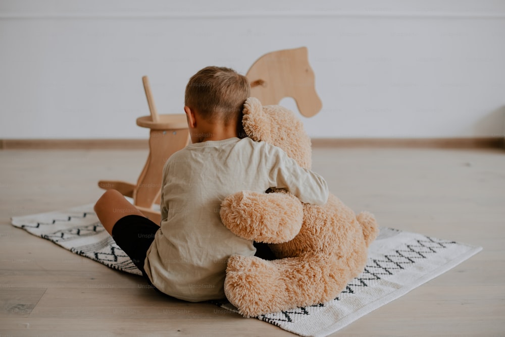 a little boy sitting on the floor with a teddy bear