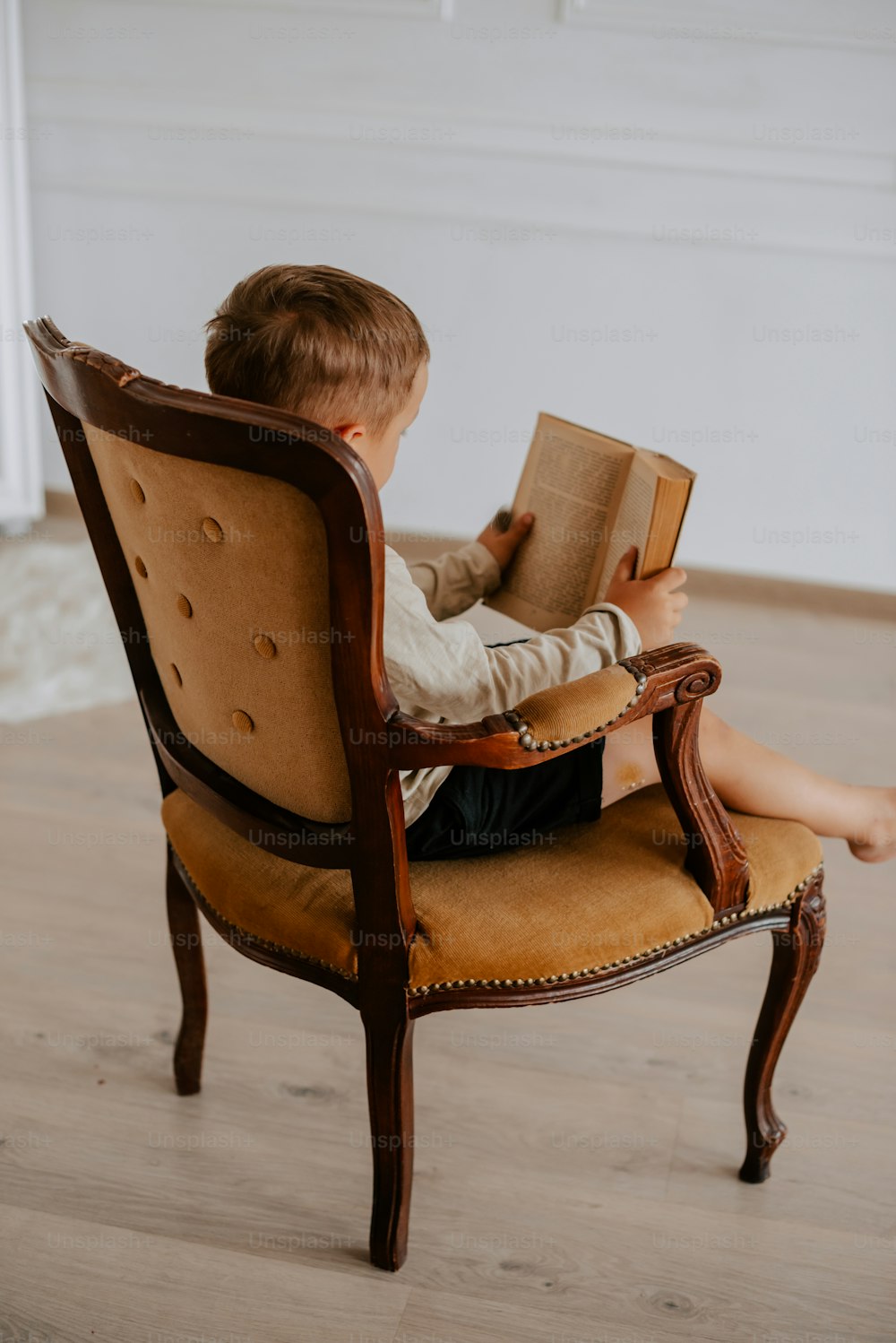 a young boy sitting in a chair reading a book