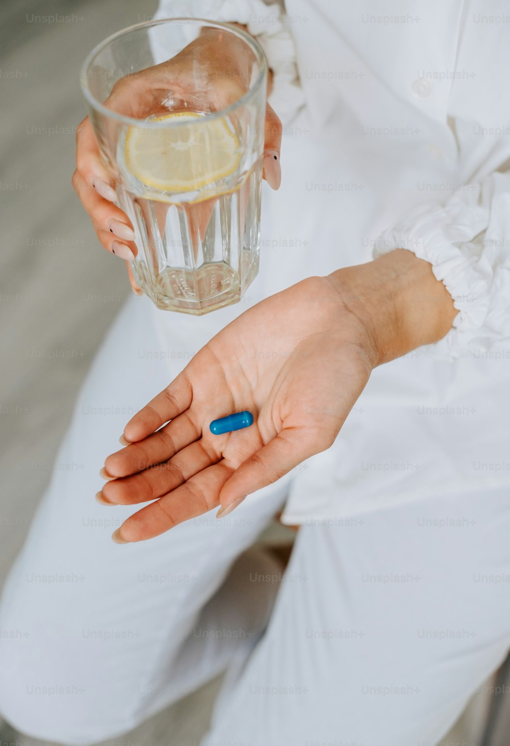 a woman holding a glass of water and a blue pill