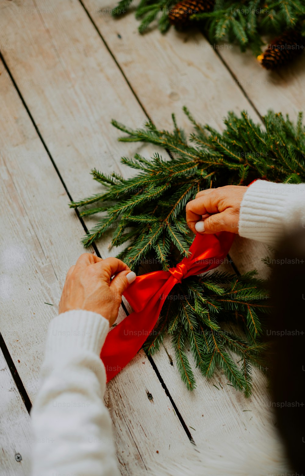 a person tying a red ribbon around a pine tree