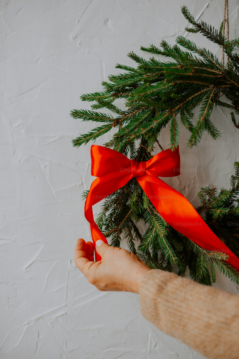 a person holding a red ribbon on a christmas wreath