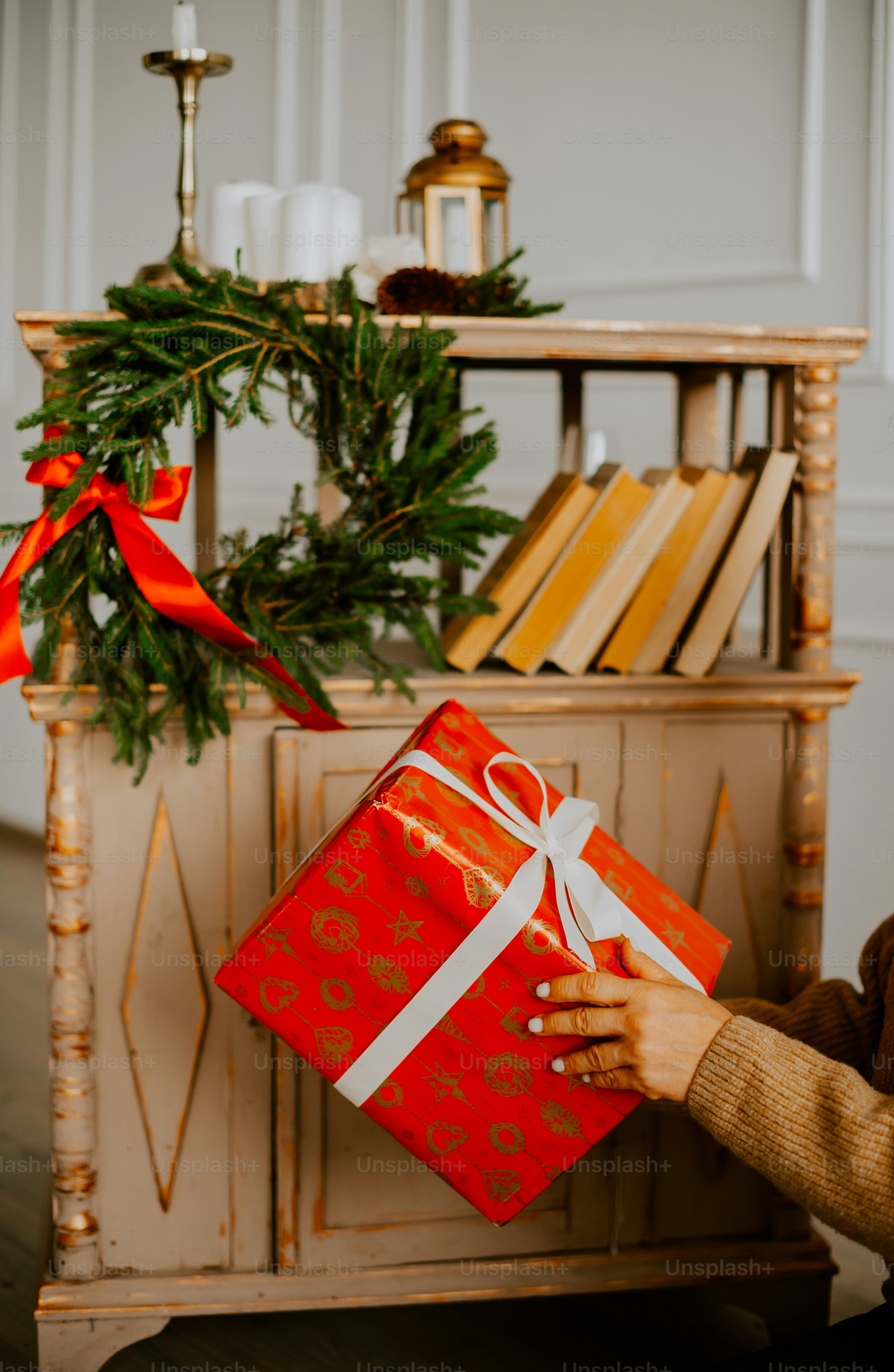 a woman holding a red gift box in front of a christmas tree