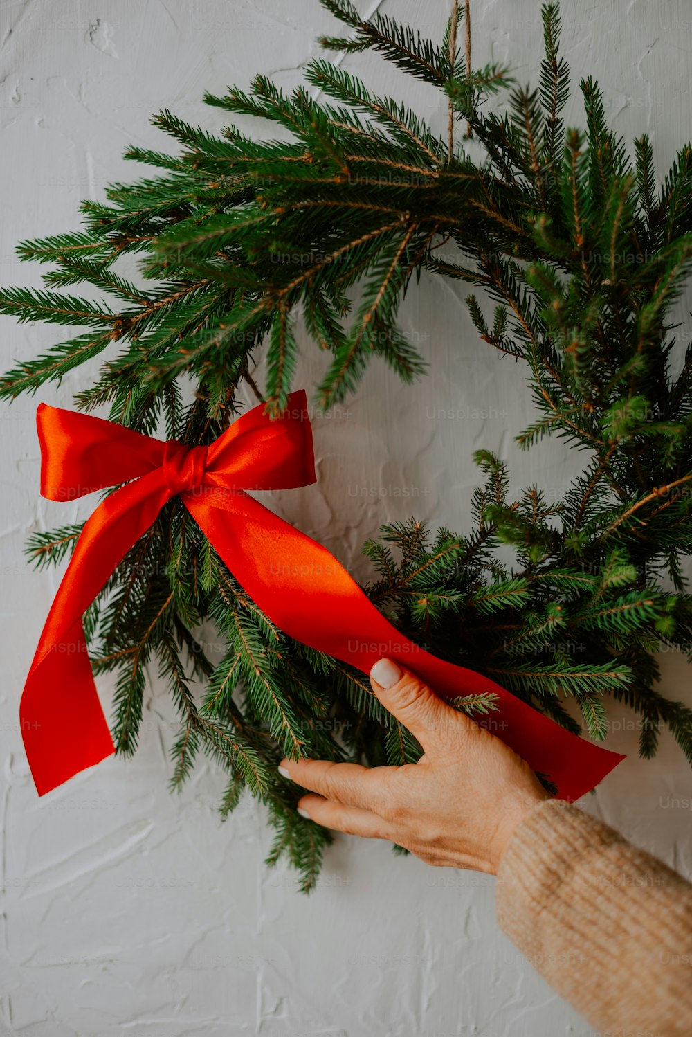 a person holding a red ribbon on a wreath