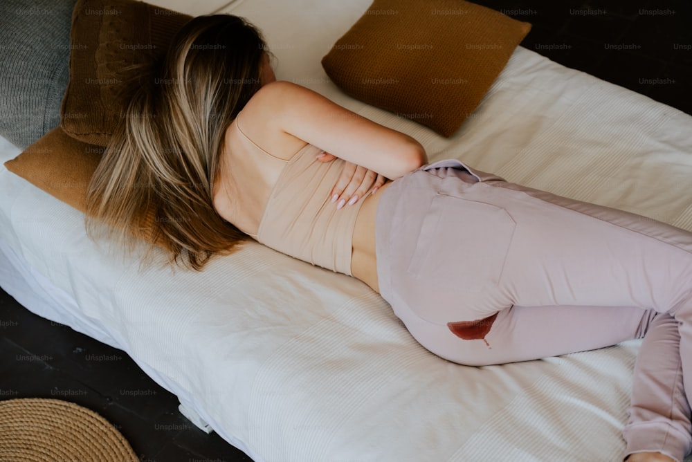 uma mulher deitada em cima de uma cama ao lado de travesseiros