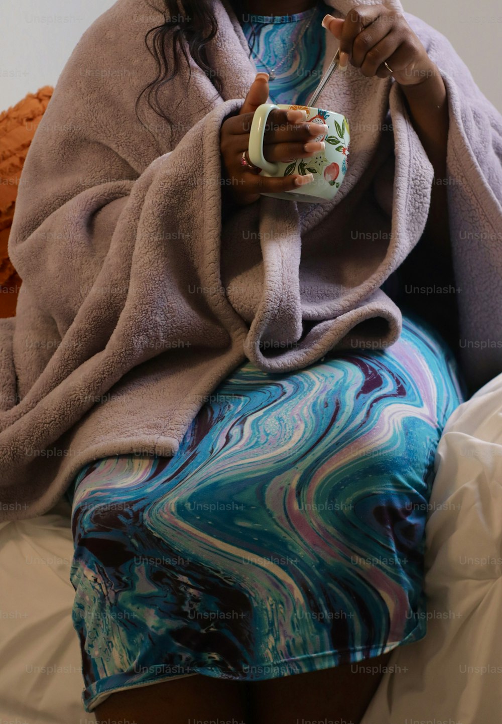 uma mulher sentada em uma cama segurando uma xícara de café