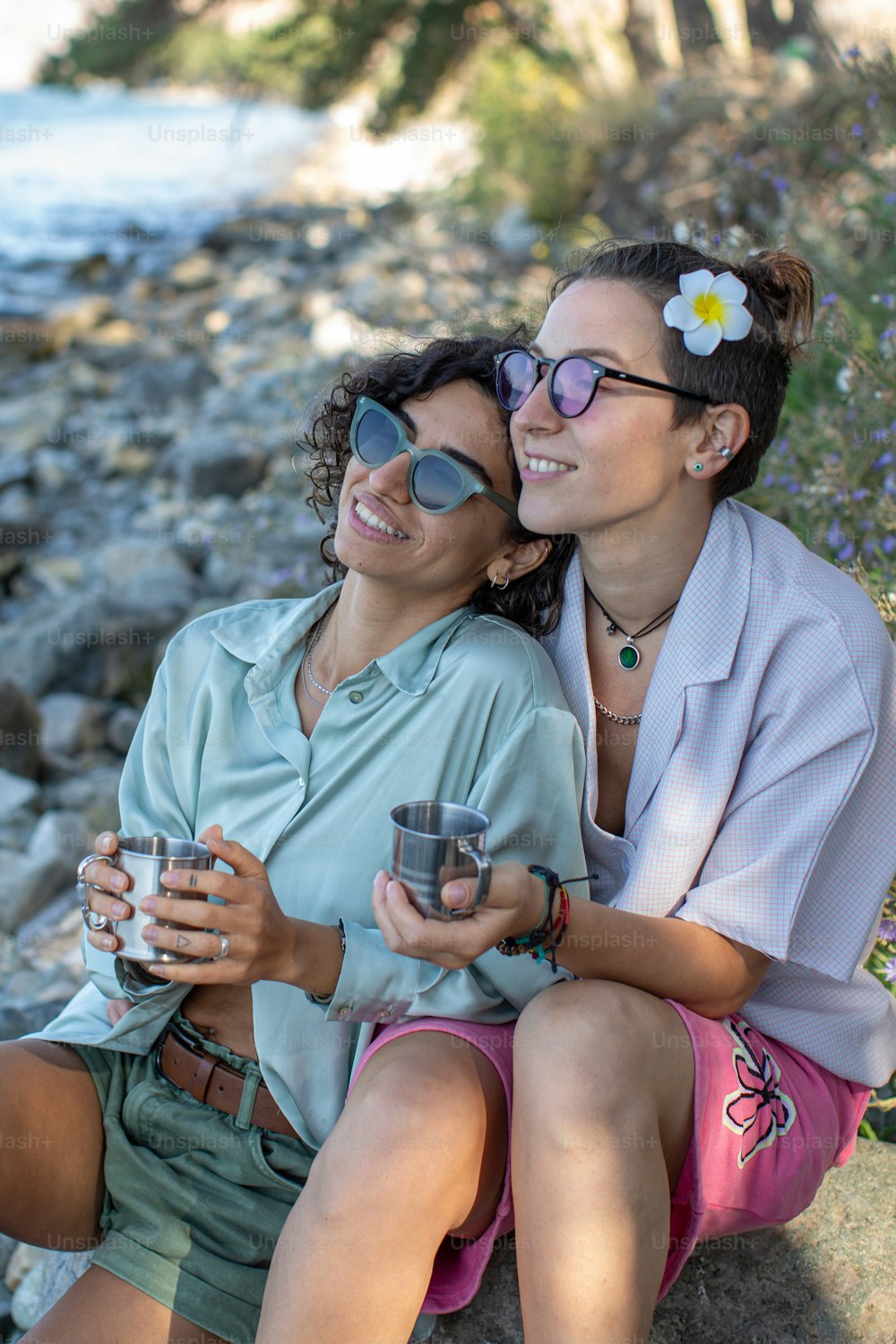 두 여자가 바위 위에 앉아 커피 한 잔을 들고 있다