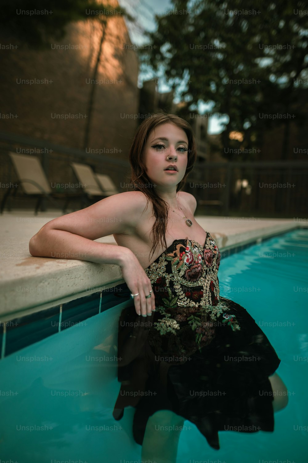 a woman in a black dress sitting on a ledge next to a swimming pool