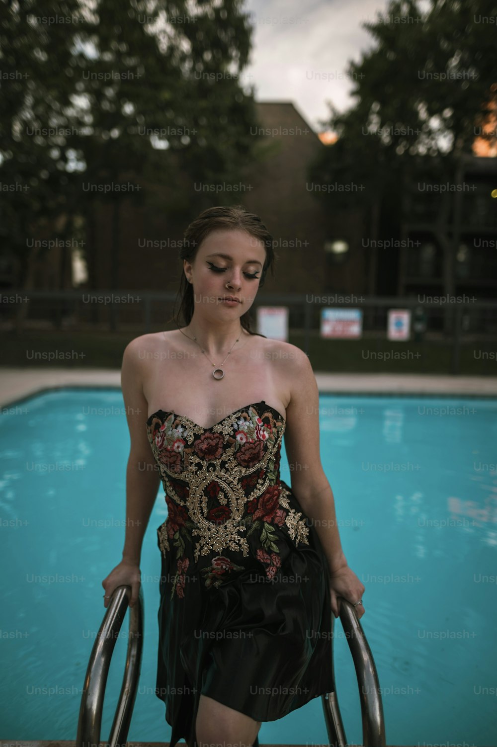 a woman in a strapless dress holding a hand rail near a swimming pool