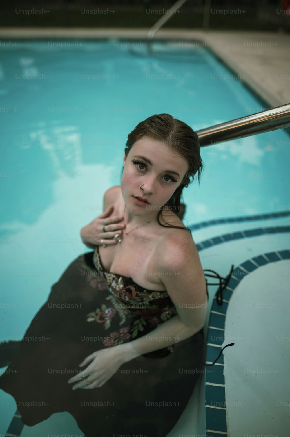 a woman in a dress sitting on the edge of a swimming pool