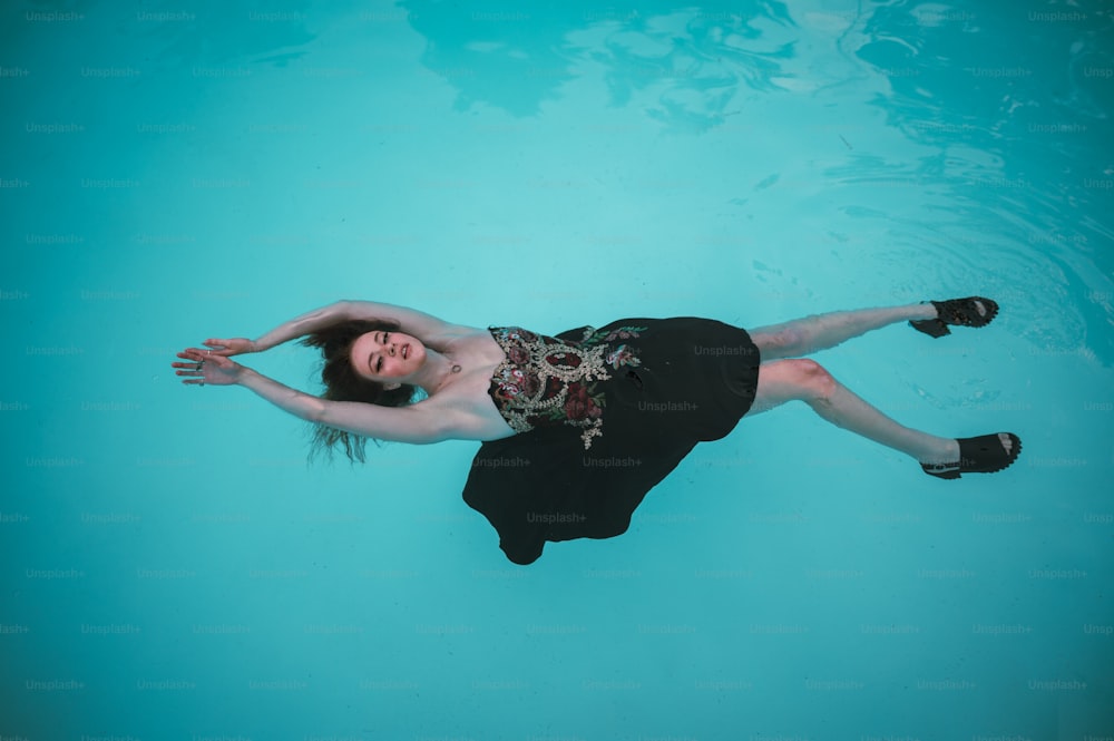 uma mulher em um vestido preto flutuando em uma piscina