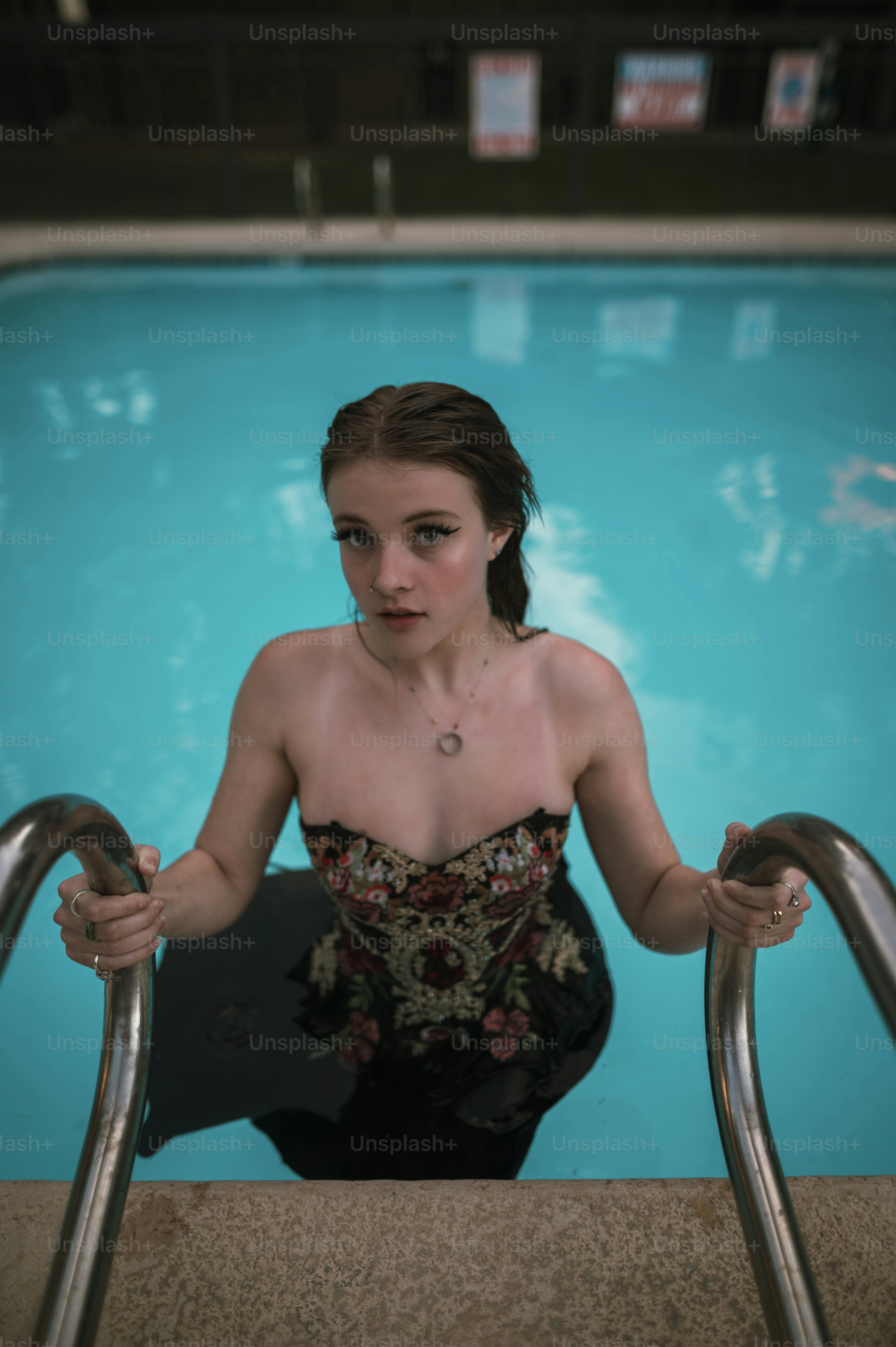 Eine Frau in einem schwarzen Kleid sitzt vor einem Swimmingpool