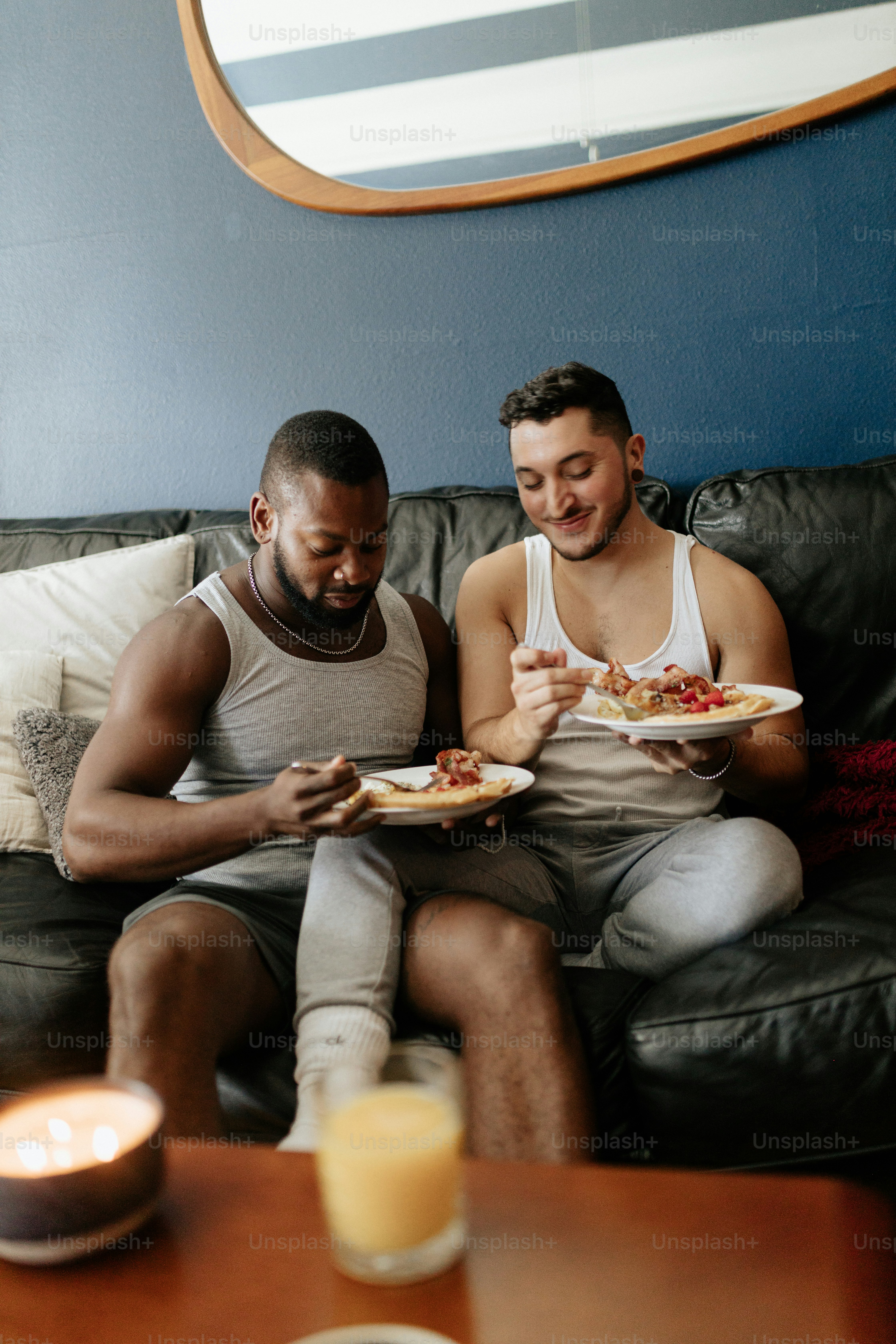 two men sitting on a couch eating pizza